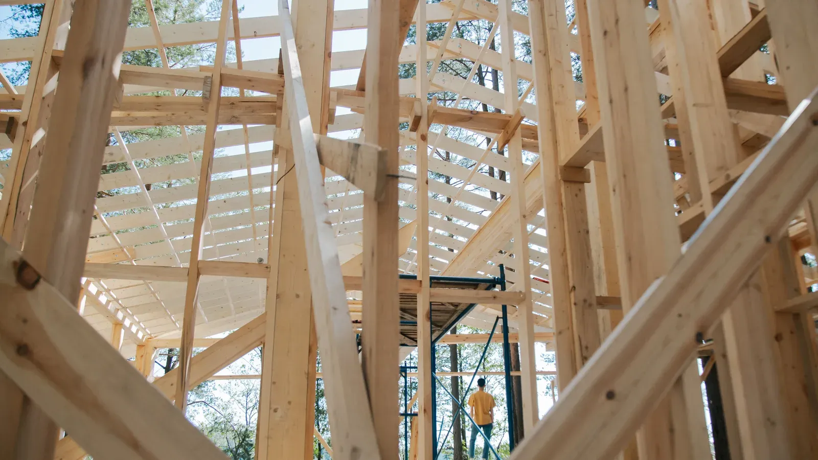 Holzrahmenbau eines Hauses im Rohbau mit Gerüst, Dachsparren und Bäumen im Hintergrund