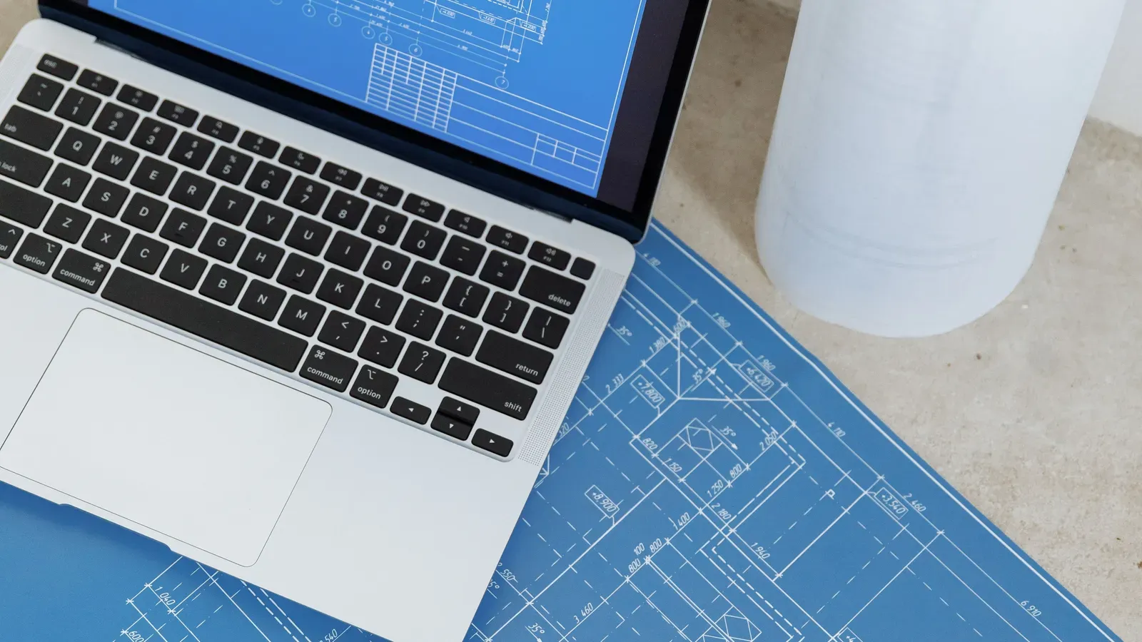 Laptop auf einem blauen Bauplan neben einer Papierrolle